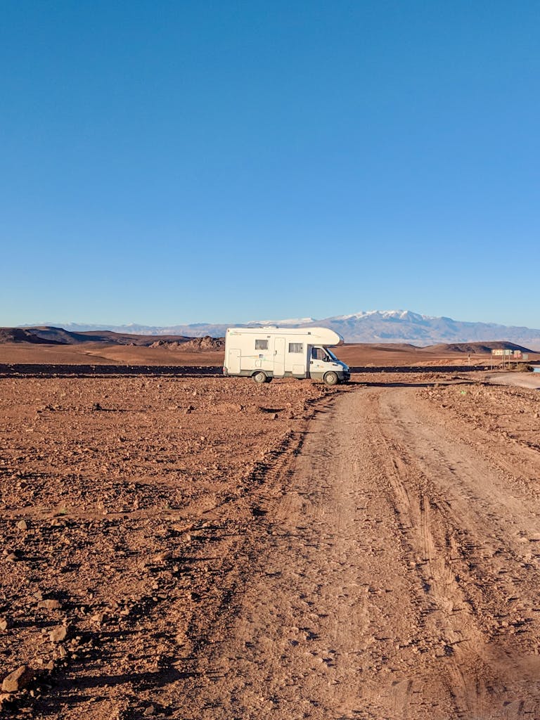 Campervan travels through arid desert landscape under clear blue sky in Morocco.