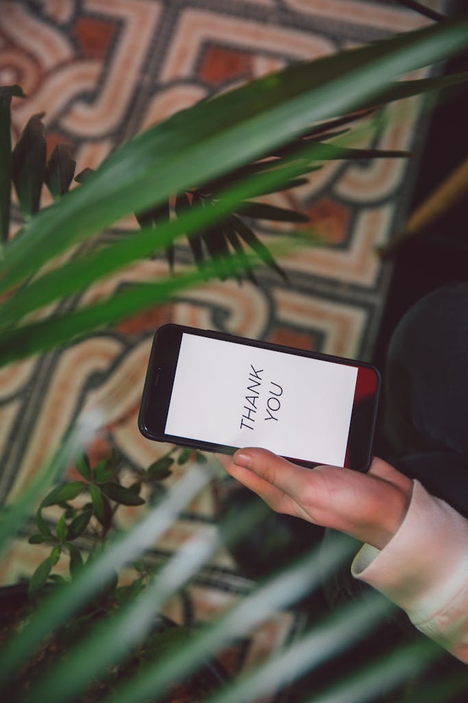 Hand holding smartphone with 'Thank You' message surrounded by lush indoor plants.